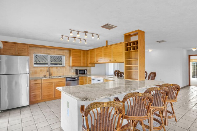 kitchen featuring light tile patterned floors, a peninsula, stainless steel appliances, and a sink