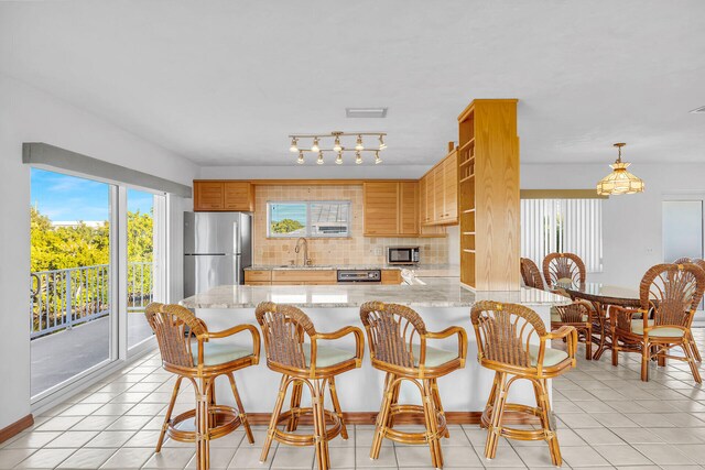 kitchen featuring tasteful backsplash, light tile patterned floors, appliances with stainless steel finishes, a peninsula, and a sink