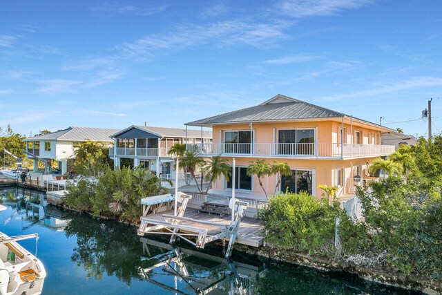 rear view of house featuring a balcony, stucco siding, a water view, boat lift, and metal roof