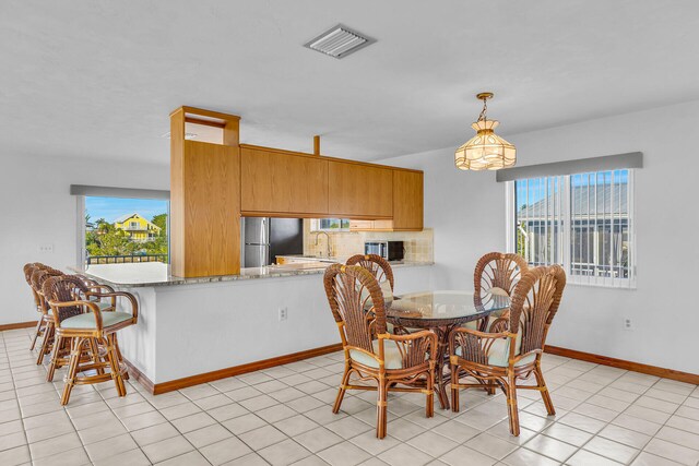 dining area with light tile patterned floors, a healthy amount of sunlight, visible vents, and baseboards