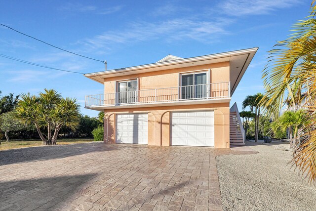 view of front of home with a balcony, an attached garage, stucco siding, stairs, and decorative driveway