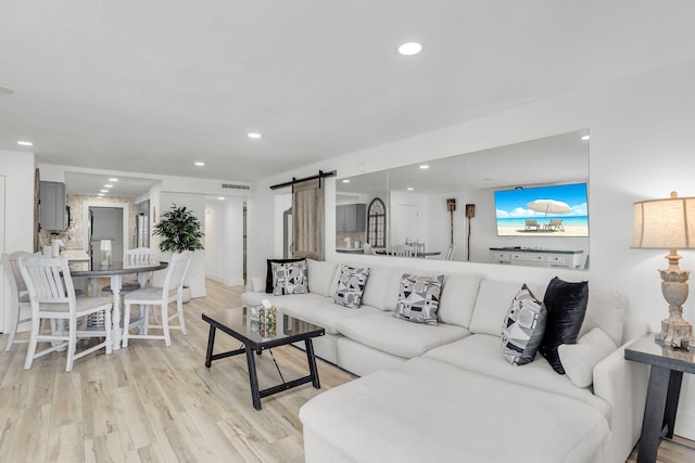 living room featuring light wood-type flooring, a barn door, visible vents, and recessed lighting