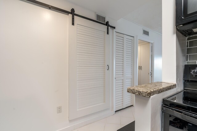 kitchen featuring light tile patterned floors, black electric range, a barn door, and visible vents