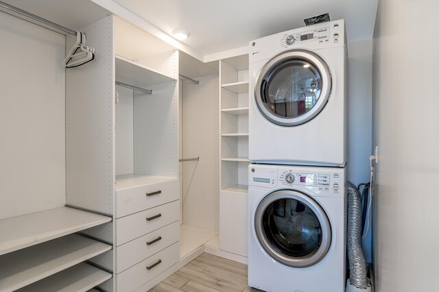 laundry area with laundry area, light wood finished floors, and stacked washer and clothes dryer