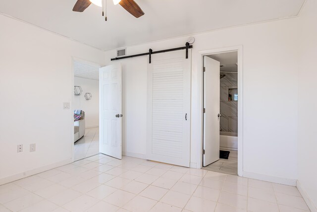 unfurnished bedroom with visible vents, a barn door, a ceiling fan, connected bathroom, and baseboards