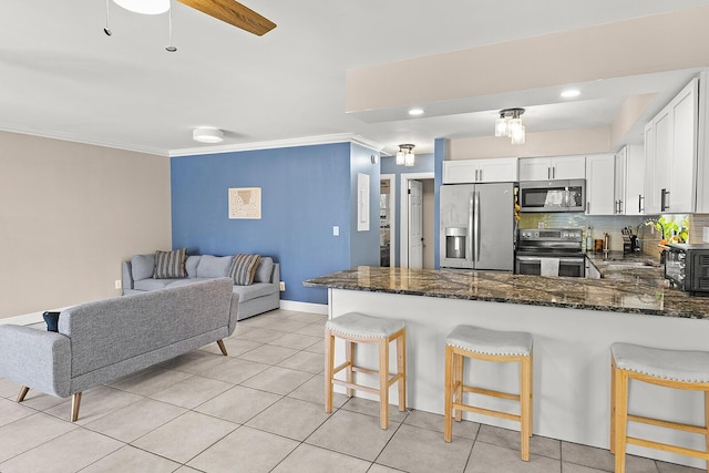 kitchen featuring stainless steel appliances, a breakfast bar, a peninsula, white cabinetry, and dark stone counters