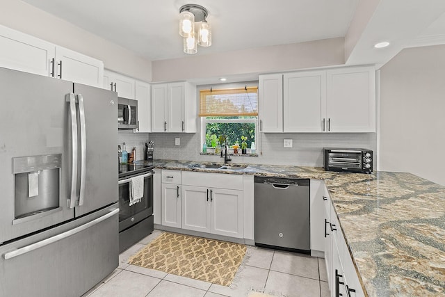 kitchen featuring stone countertops, tasteful backsplash, white cabinets, stainless steel appliances, and a sink