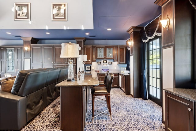 kitchen with dark brown cabinetry, a center island, a kitchen breakfast bar, light stone countertops, and glass insert cabinets