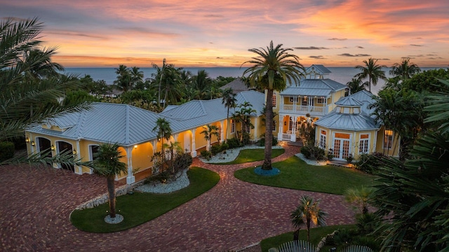 view of front of property with a balcony, curved driveway, a water view, a standing seam roof, and french doors