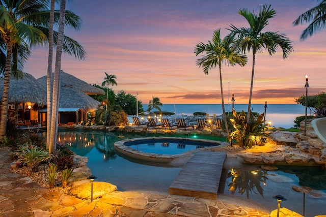 pool at dusk with a pool with connected hot tub and a water view