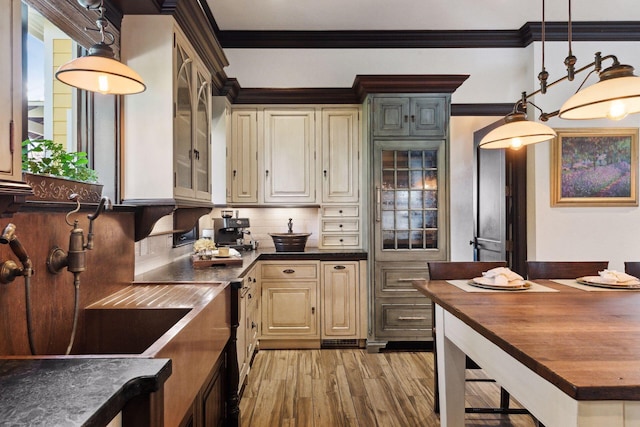 kitchen featuring decorative light fixtures, crown molding, cream cabinets, glass insert cabinets, and light wood-style floors