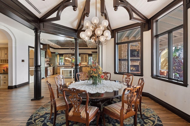 dining room featuring arched walkways, ornate columns, wood finished floors, a chandelier, and baseboards