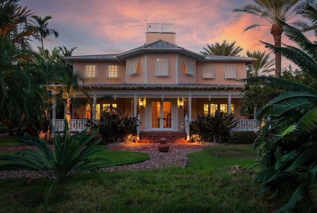 view of front of home with a yard, a chimney, a porch, and french doors