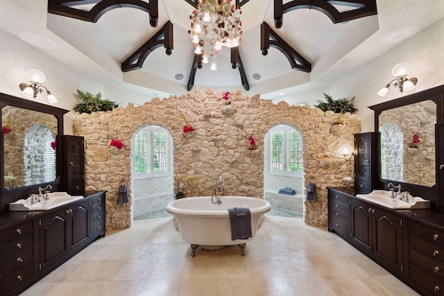 bathroom featuring a freestanding bath, high vaulted ceiling, two vanities, and a sink