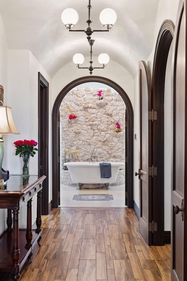 foyer entrance with arched walkways, dark wood finished floors, lofted ceiling, an inviting chandelier, and baseboards