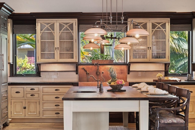 kitchen with cream cabinetry, dark countertops, glass insert cabinets, an island with sink, and a kitchen bar