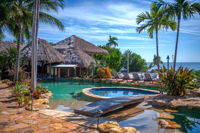 view of swimming pool with a water view, a patio area, and a pool with connected hot tub