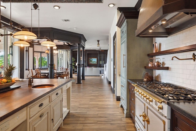 kitchen with white range with gas cooktop, tasteful backsplash, custom range hood, wood counters, and cream cabinetry