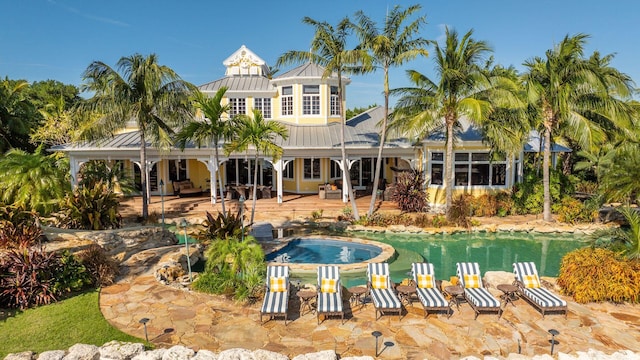 rear view of house with metal roof, a standing seam roof, a patio area, and a pool with connected hot tub