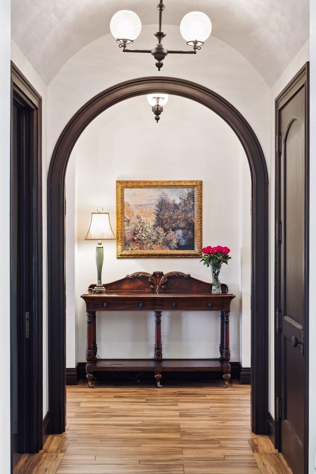 hallway featuring light wood-style floors, vaulted ceiling, and baseboards