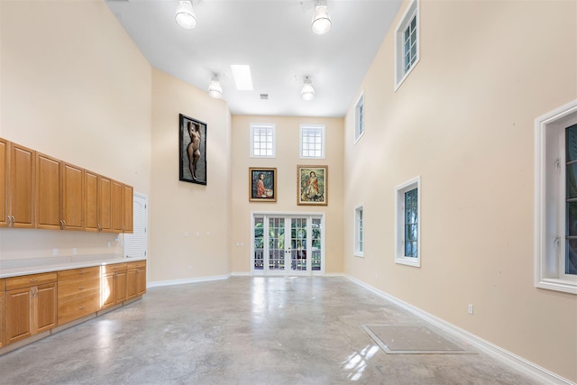 unfurnished living room with finished concrete floors, a skylight, a high ceiling, and baseboards