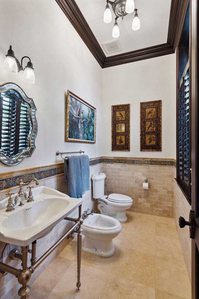 bathroom featuring wainscoting, toilet, ornamental molding, a bidet, and tile walls