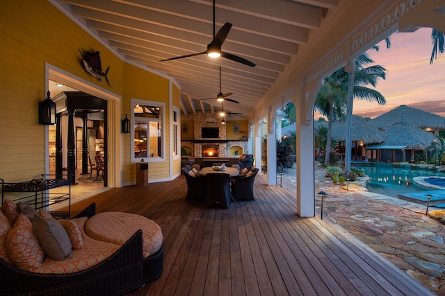 deck featuring a lit fireplace, an outdoor pool, and a ceiling fan