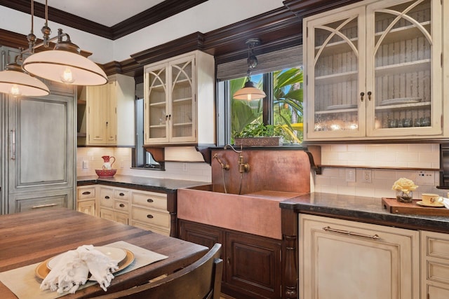 kitchen with tasteful backsplash, hanging light fixtures, cream cabinets, glass insert cabinets, and ornamental molding