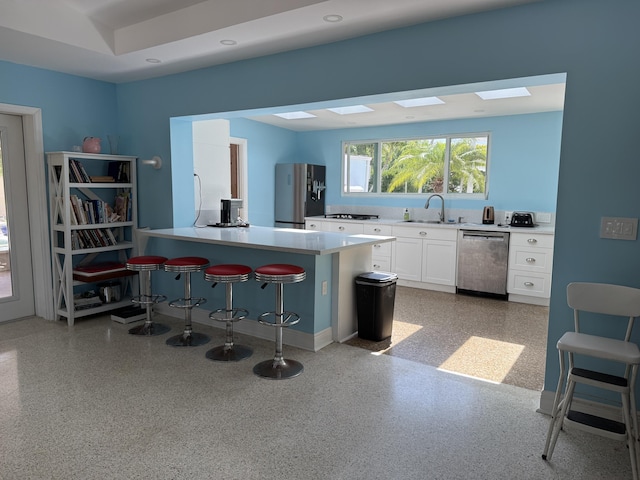 kitchen with a breakfast bar, a sink, white cabinetry, light countertops, and appliances with stainless steel finishes