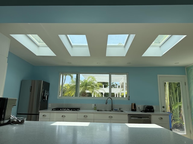 kitchen with a sink, stainless steel appliances, a skylight, and white cabinetry