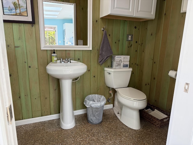 bathroom with toilet, wooden walls, baseboards, and a sink