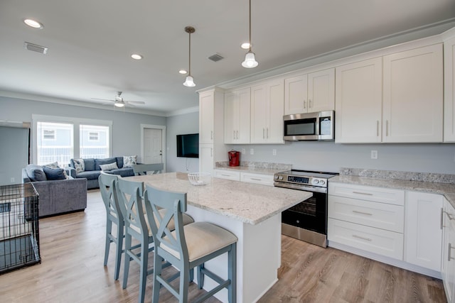 kitchen featuring pendant lighting, stainless steel appliances, open floor plan, white cabinets, and a kitchen bar