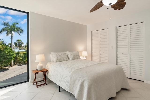 bedroom featuring two closets, light tile patterned floors, access to outside, and a wall of windows