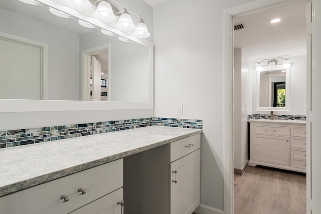 bathroom with decorative backsplash, visible vents, baseboards, wood finished floors, and vanity