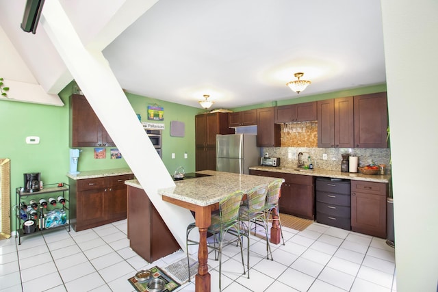 kitchen with light tile patterned flooring, backsplash, freestanding refrigerator, and light stone countertops