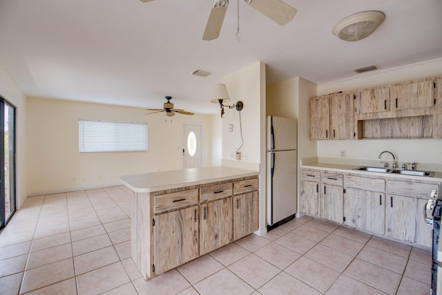 kitchen with a sink, light tile patterned flooring, ceiling fan, freestanding refrigerator, and light brown cabinets