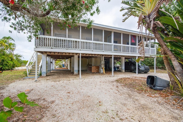 view of front of property with stairs, a carport, a sunroom, and dirt driveway