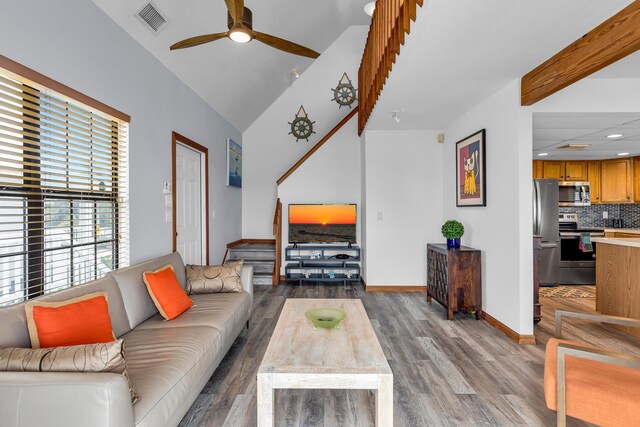 living area featuring light wood finished floors, visible vents, baseboards, ceiling fan, and vaulted ceiling