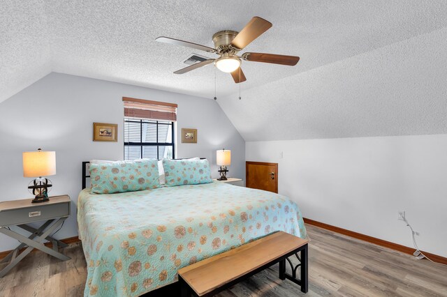 bedroom with visible vents, vaulted ceiling, a textured ceiling, and wood finished floors