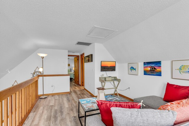 living room featuring visible vents, attic access, vaulted ceiling, a textured ceiling, and wood finished floors