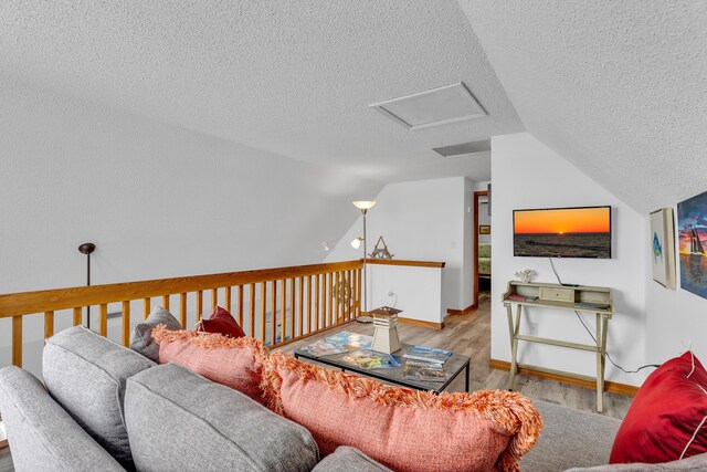 living area with lofted ceiling, a textured ceiling, wood finished floors, baseboards, and attic access