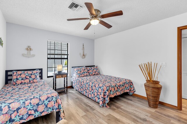 bedroom with baseboards, visible vents, ceiling fan, wood finished floors, and a textured ceiling