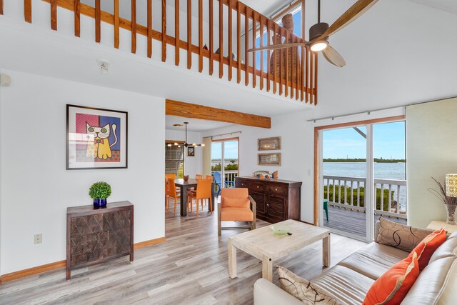 living room with ceiling fan with notable chandelier, a high ceiling, a water view, wood finished floors, and baseboards