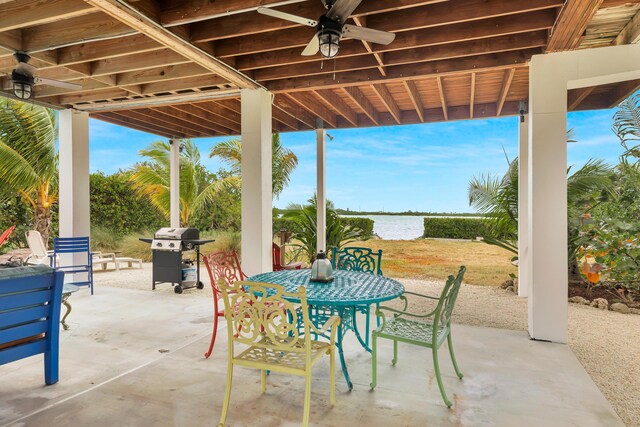 view of patio with a water view, outdoor dining area, a ceiling fan, and area for grilling