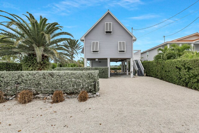 rear view of property featuring gravel driveway, stairway, and a carport