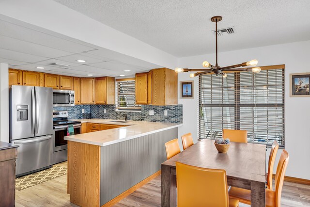 kitchen featuring light wood finished floors, visible vents, a peninsula, stainless steel appliances, and a sink