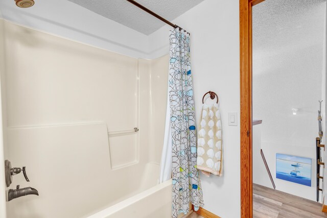 bathroom with shower / bathtub combination with curtain, a textured ceiling, and wood finished floors