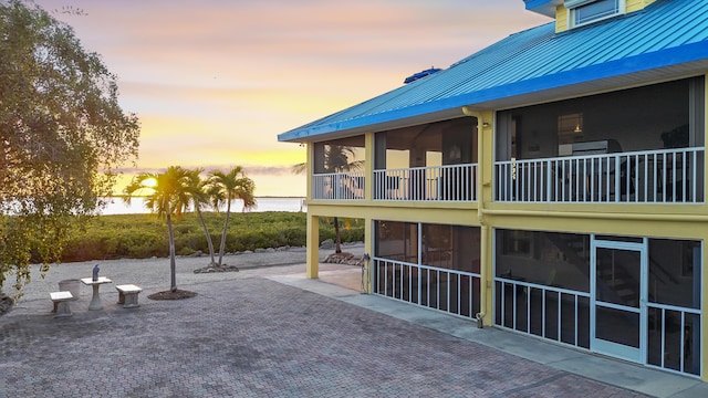 exterior space featuring a sunroom, a patio area, metal roof, and a water view