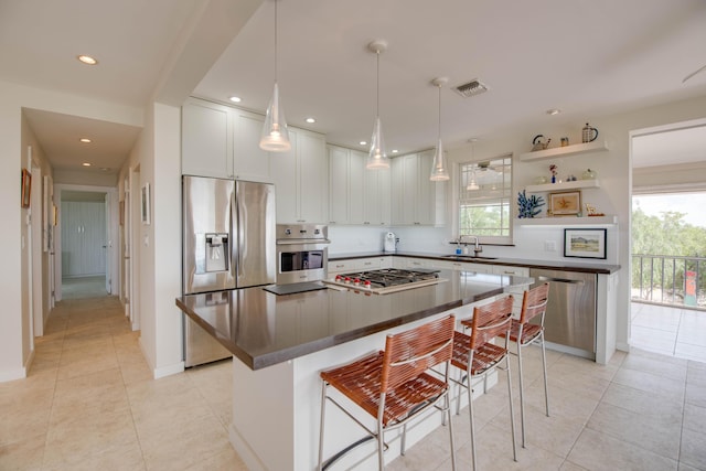 kitchen featuring white cabinetry, appliances with stainless steel finishes, a center island, dark countertops, and a kitchen bar