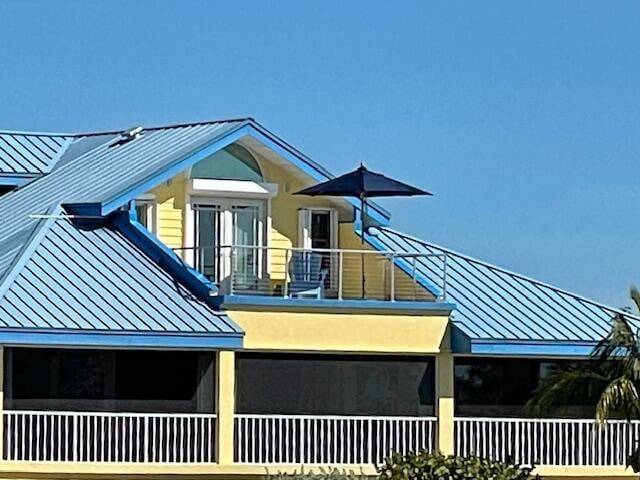 view of side of home with a balcony, a standing seam roof, metal roof, and stucco siding